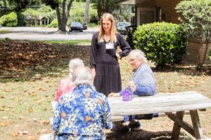 Young lady standing by a picnic table. talking to a group of elderly people