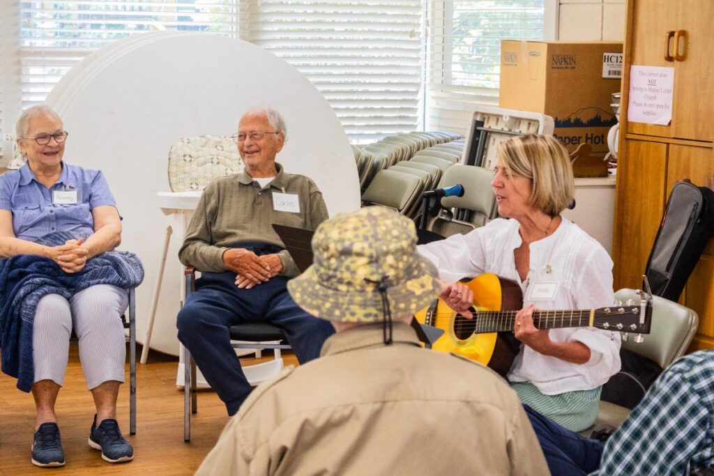 A lady playing a guitar for a group of dementia patients.